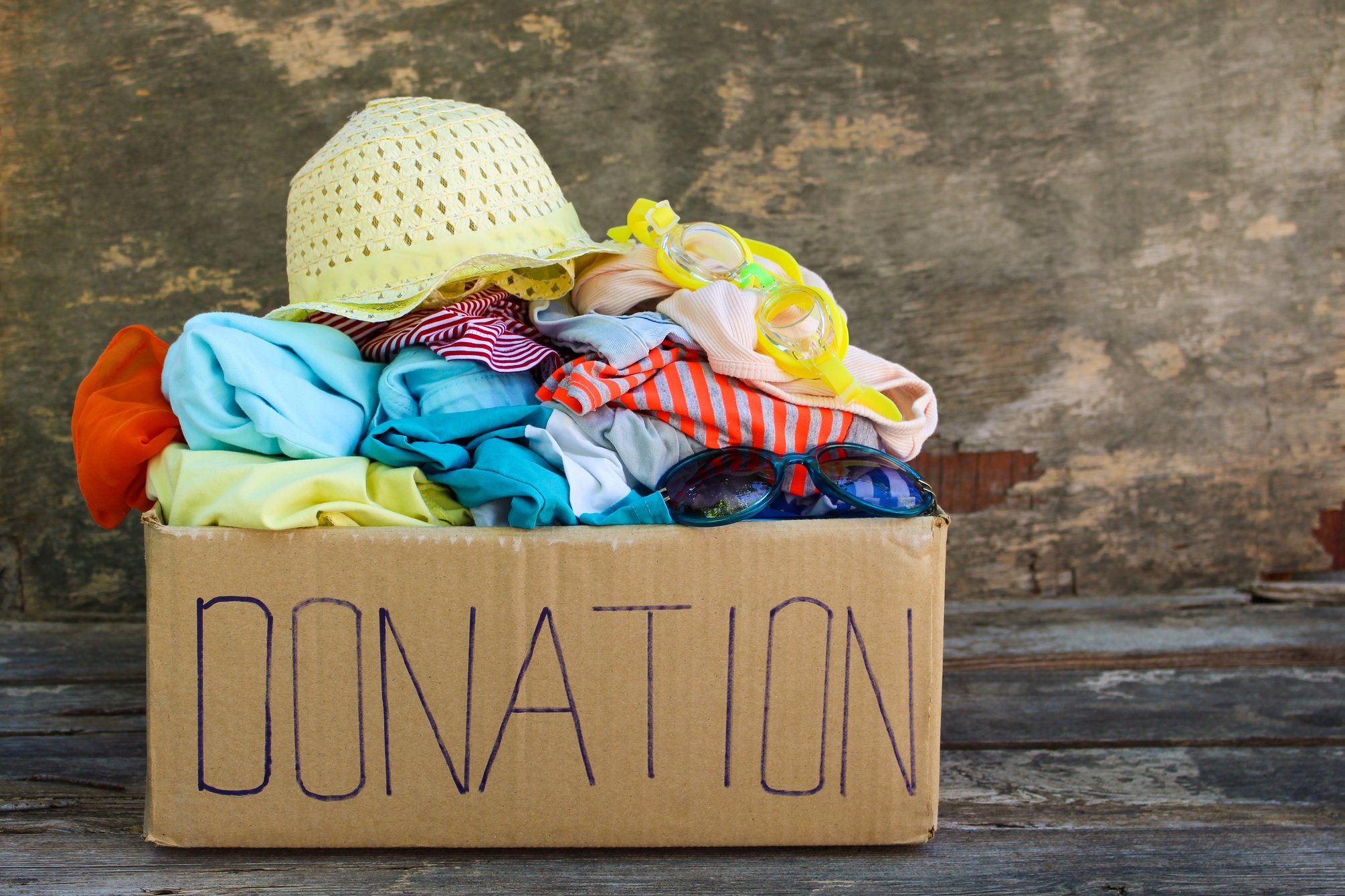 Donation box with summer clothes on the old wooden backgroun