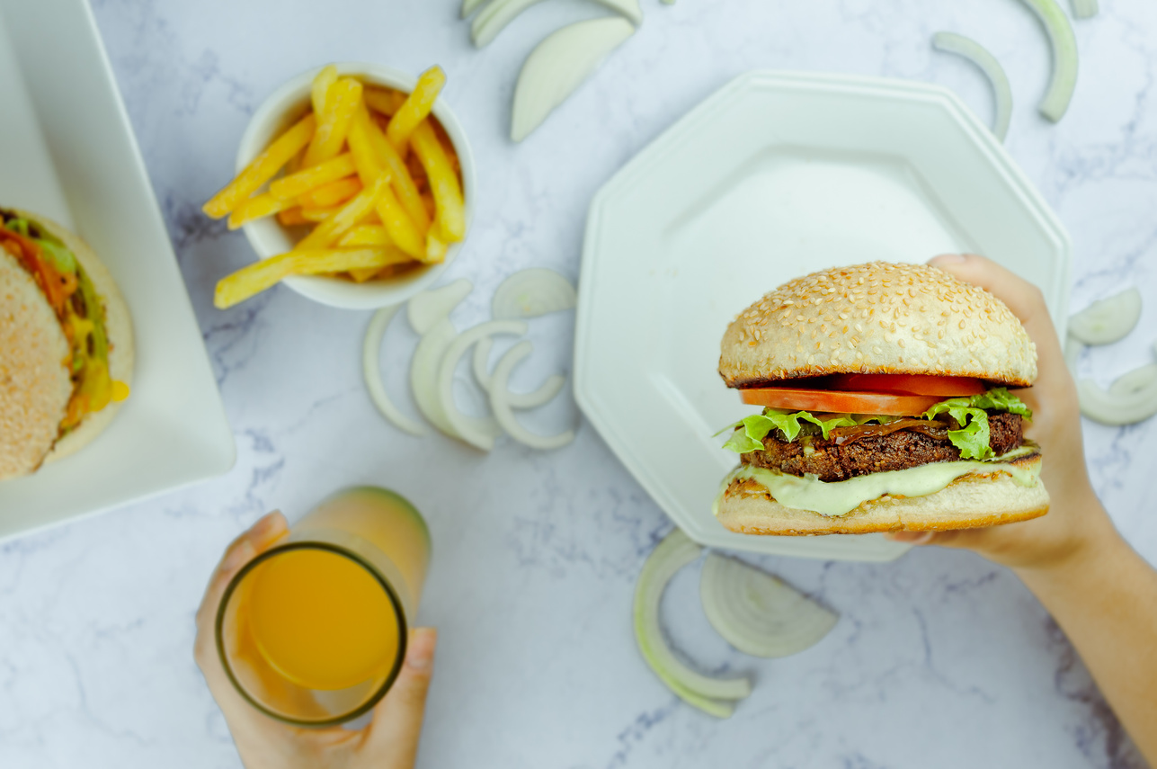 Anonymous person eating hamburger and drinking juice